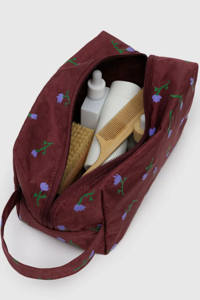 Maroon toiletry bag with floral patterns containing grooming items on a white background