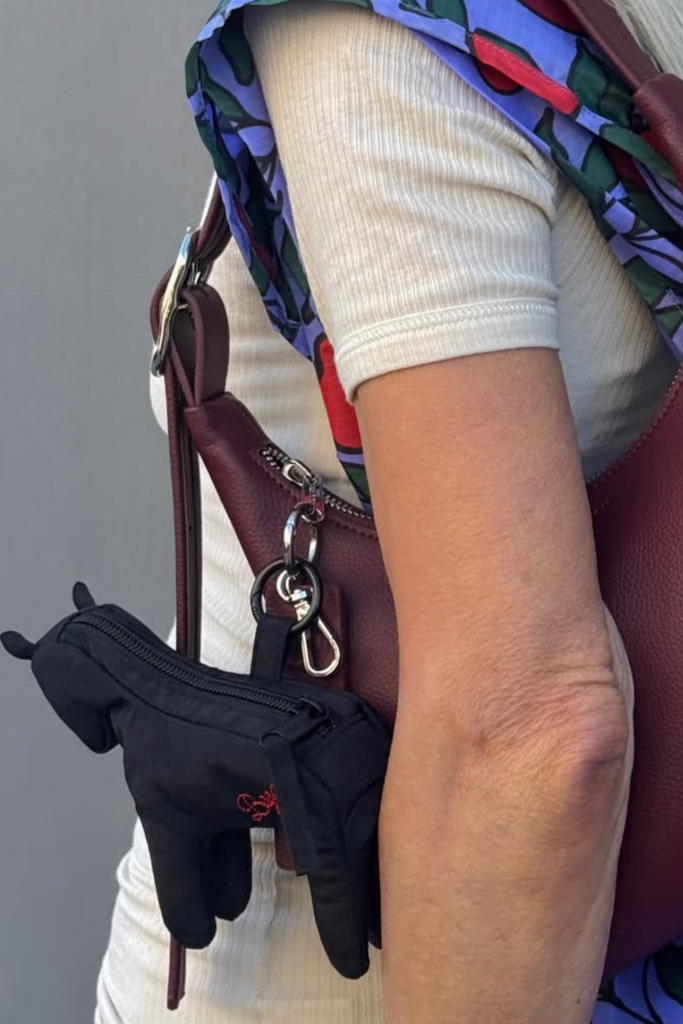 Person holding a maroon handbag with a keychain and black gloves, wearing a colorful scarf.
