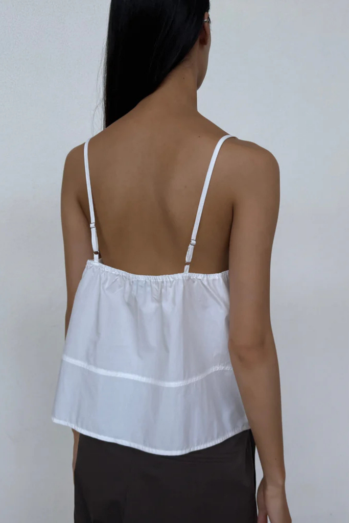 Woman wearing a white spaghetti strap top against a plain background