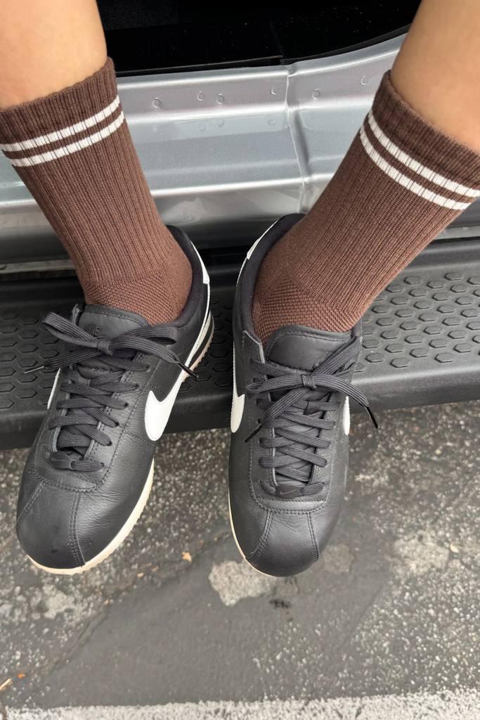 Person wearing black sneakers and brown socks with white stripes stepping onto a car.