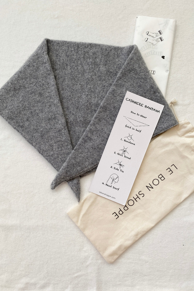Gray cashmere bandana with a white label and beige drawstring bag on a light gray background